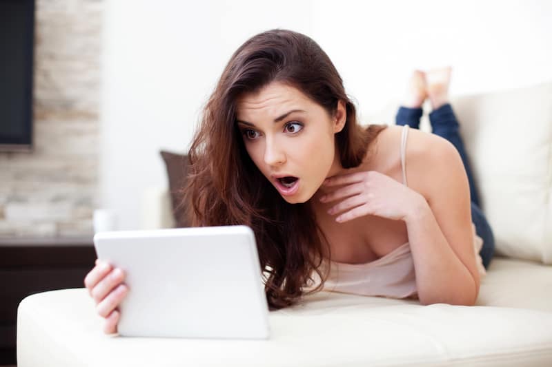 Eine junge Frau schaut mit geschocktem Gesichtsausdruck auf ein Tablet